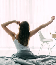 back view young woman stretching unmade bed after waking up looking city view window
